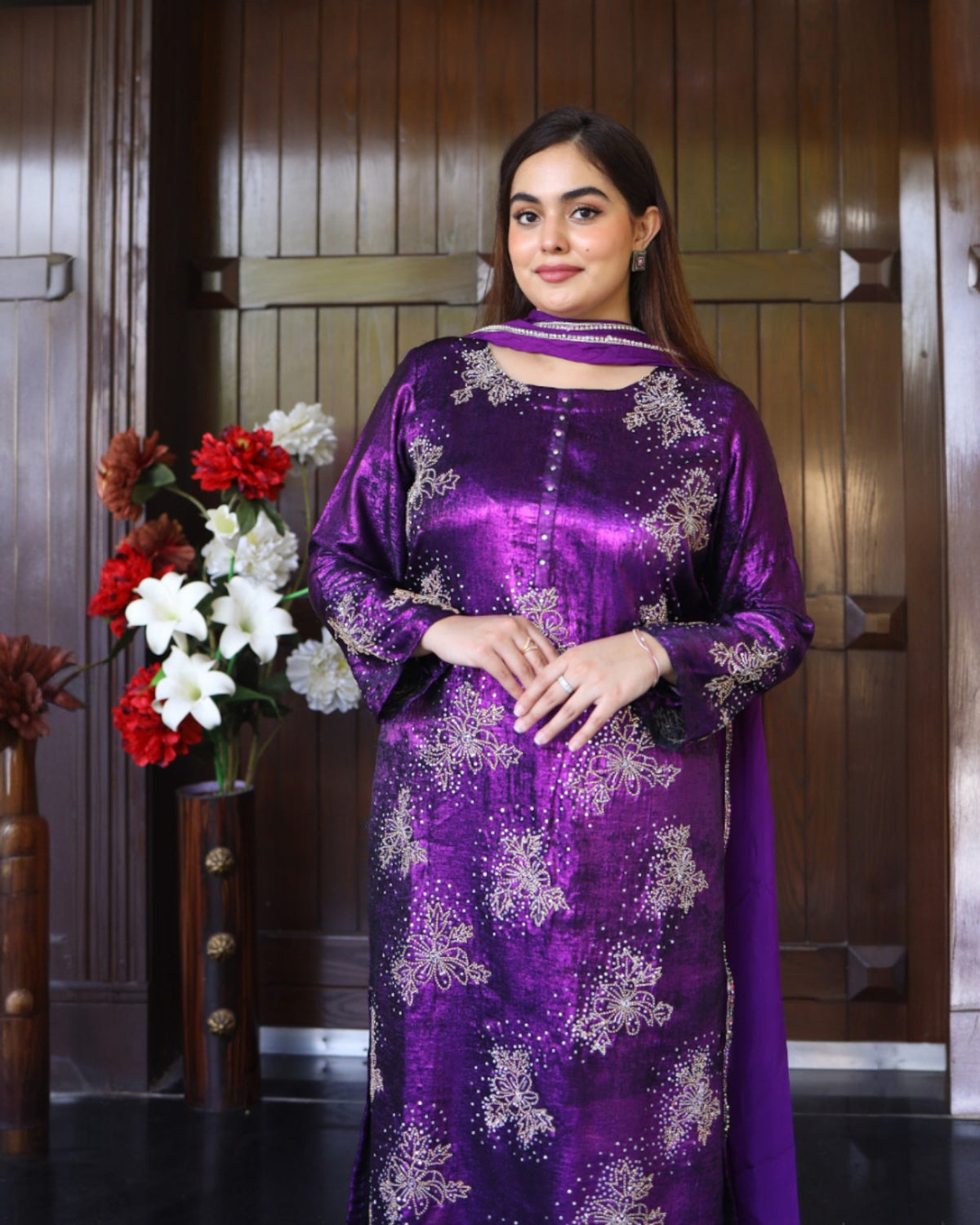 Woman wearing a purple traditional outfit with floral patterns in a room with wooden paneling.