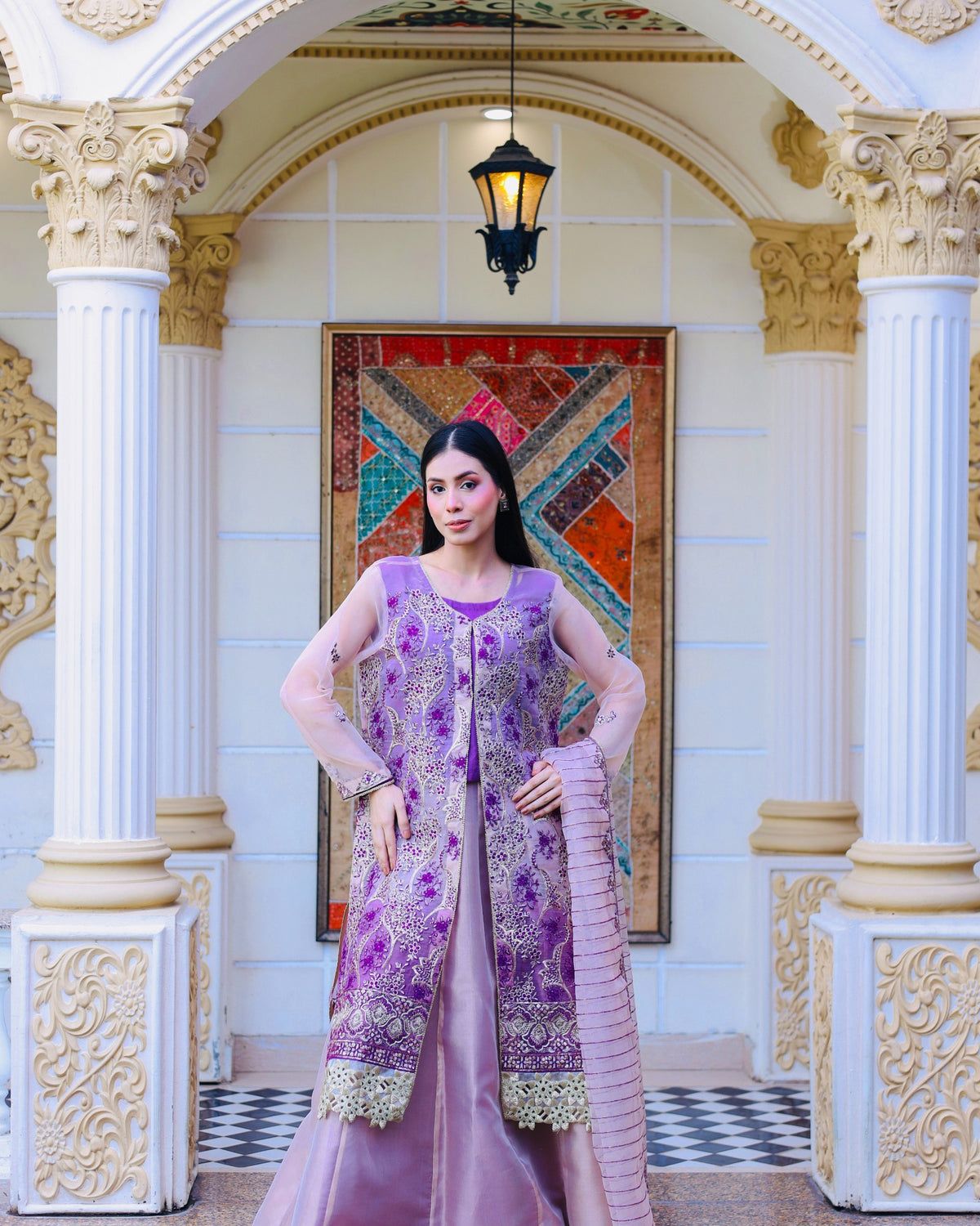 Woman in a purple traditional outfit standing in an ornate interior setting.