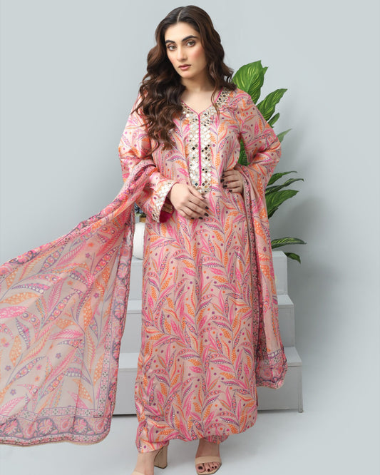 Woman wearing a pink and orange patterned dress with a scarf, standing against a light gray background.