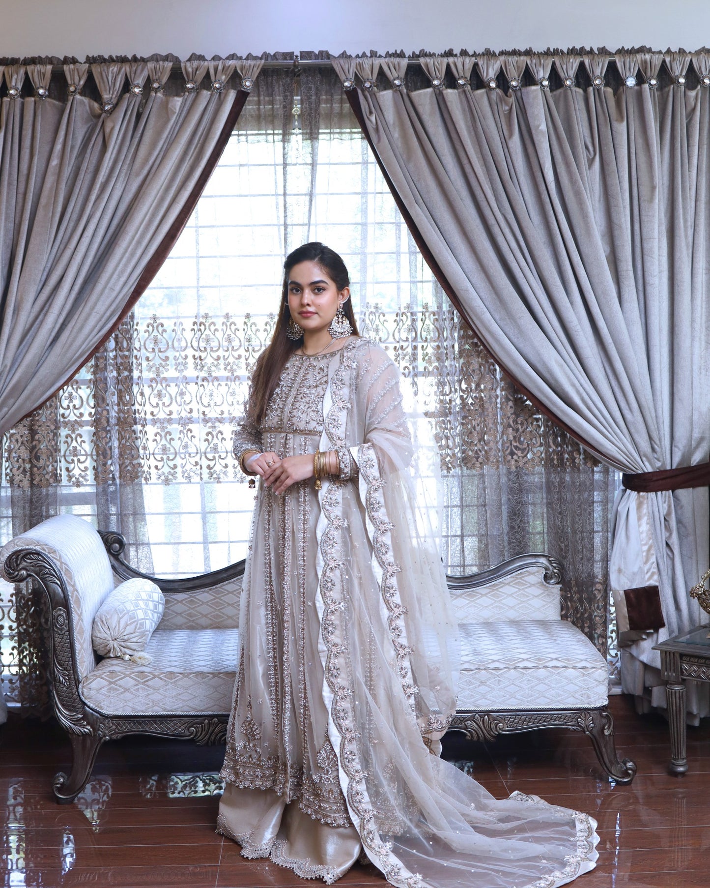 Woman in a traditional outfit standing in a decorated room with curtains and furniture.