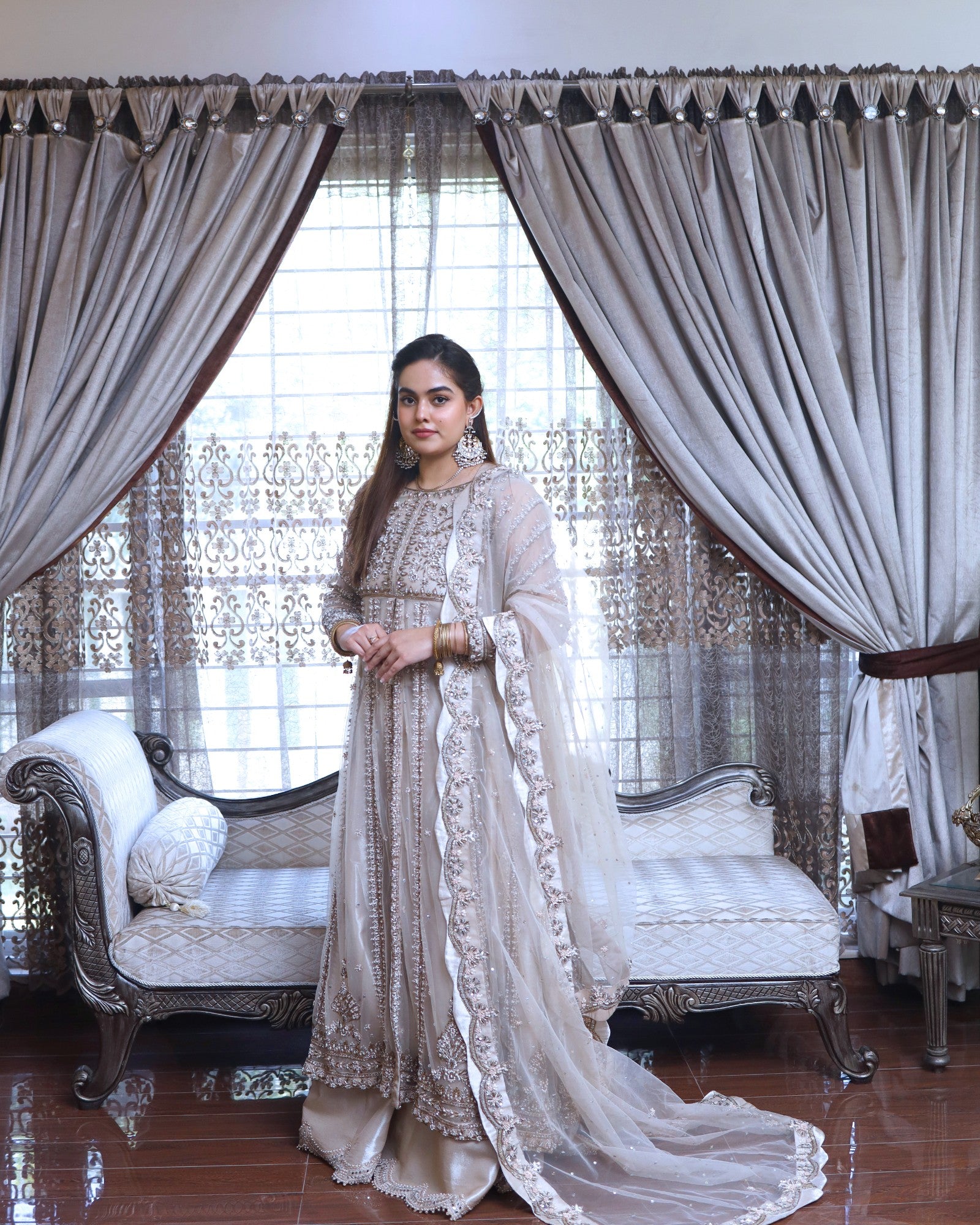 Woman in a traditional outfit standing in a decorated room with curtains and furniture.