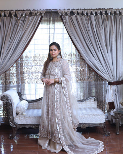 Woman in a traditional outfit standing in a decorated room with curtains and furniture.