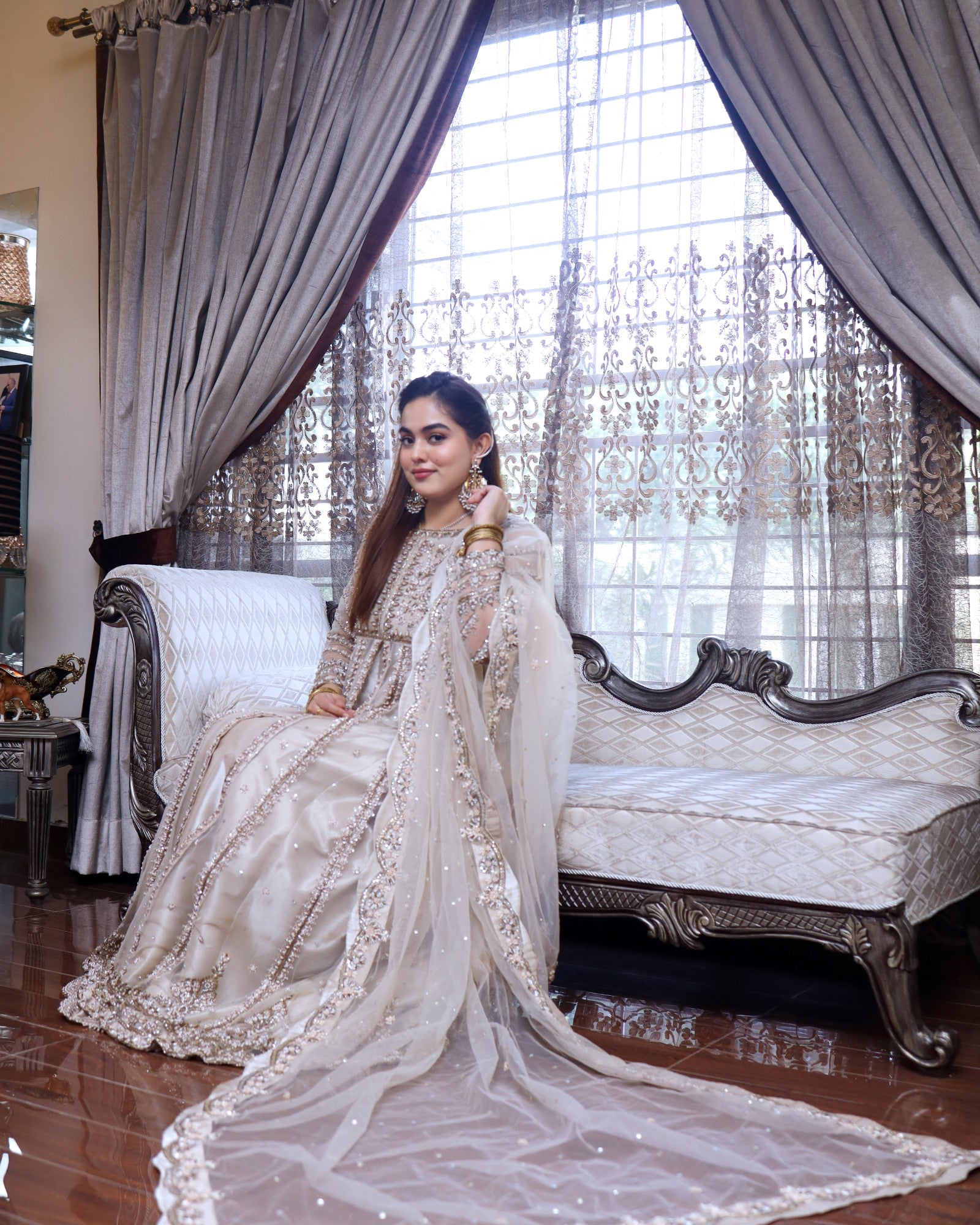 Woman in a traditional outfit sitting on an ornate sofa with decorative curtains in the background