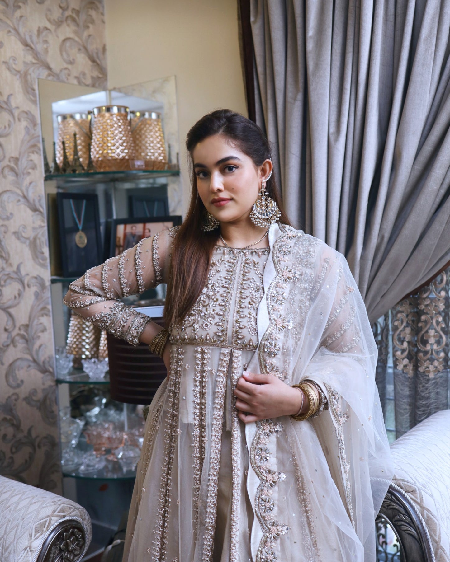 Woman in an embroidered traditional outfit standing in a decorated room.
