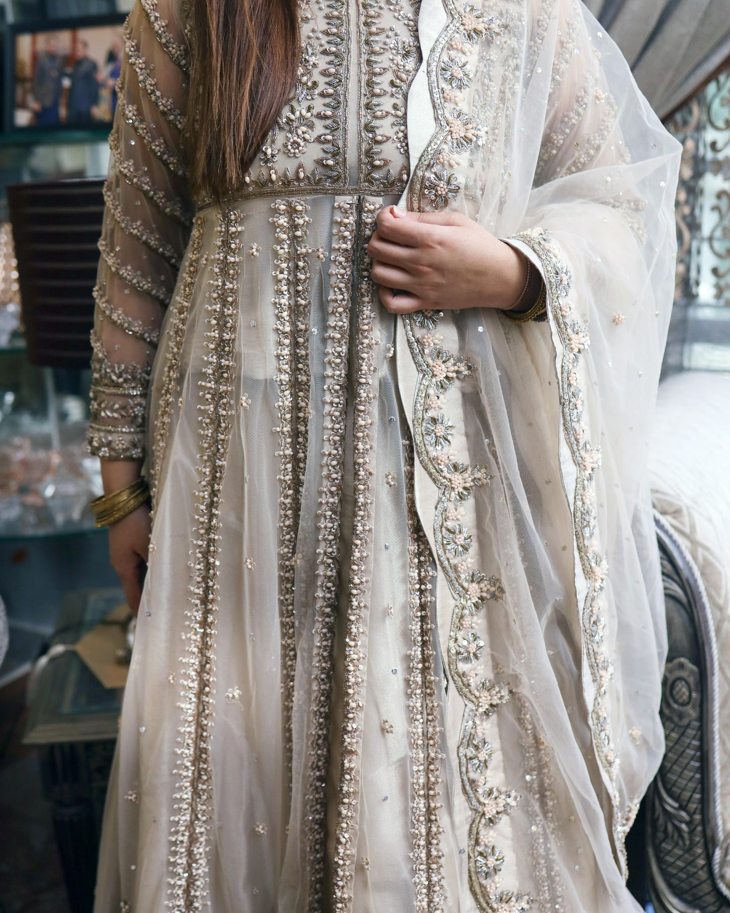 Close-up of a person wearing an intricately designed beige and gold traditional outfit with a sheer overlay.
