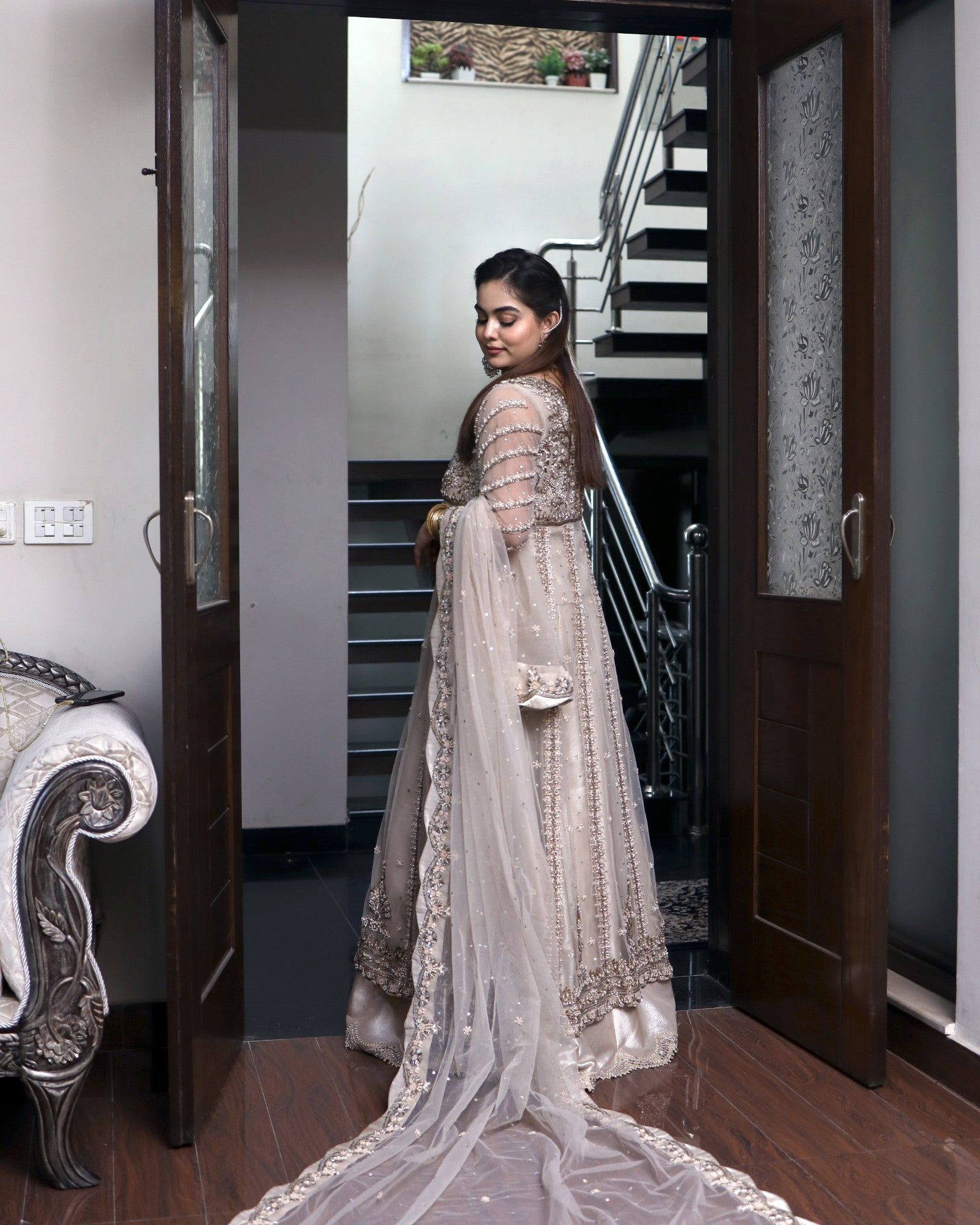 Woman in a traditional outfit standing in a home interior with a staircase.