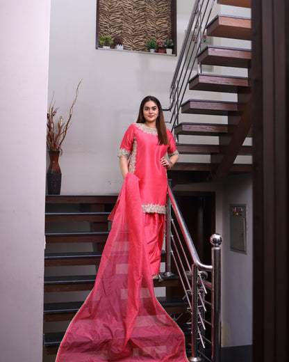 Woman in a pink saree standing in a modern interior setting with stairs.