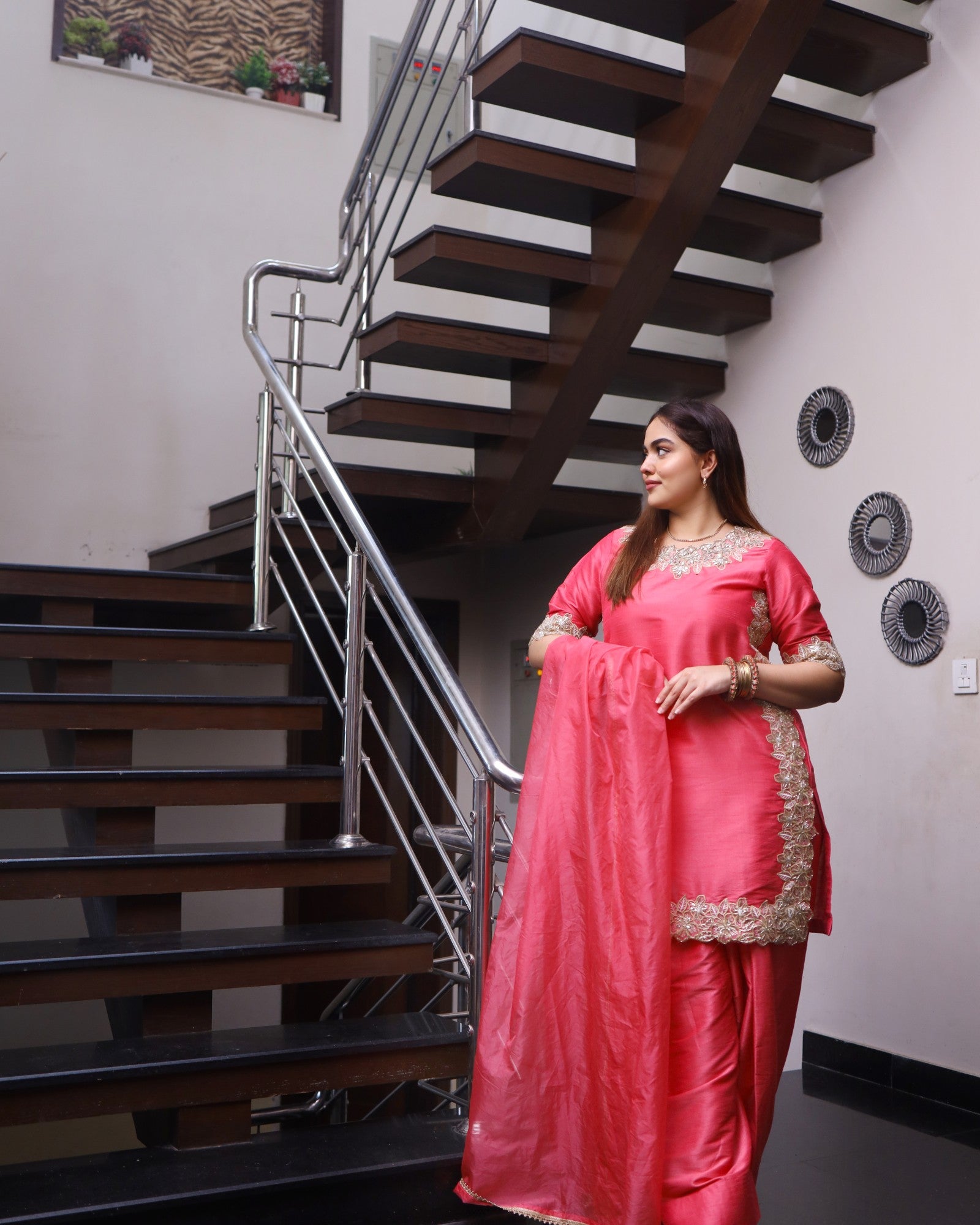 Woman in a pink saree standing in front of a staircase