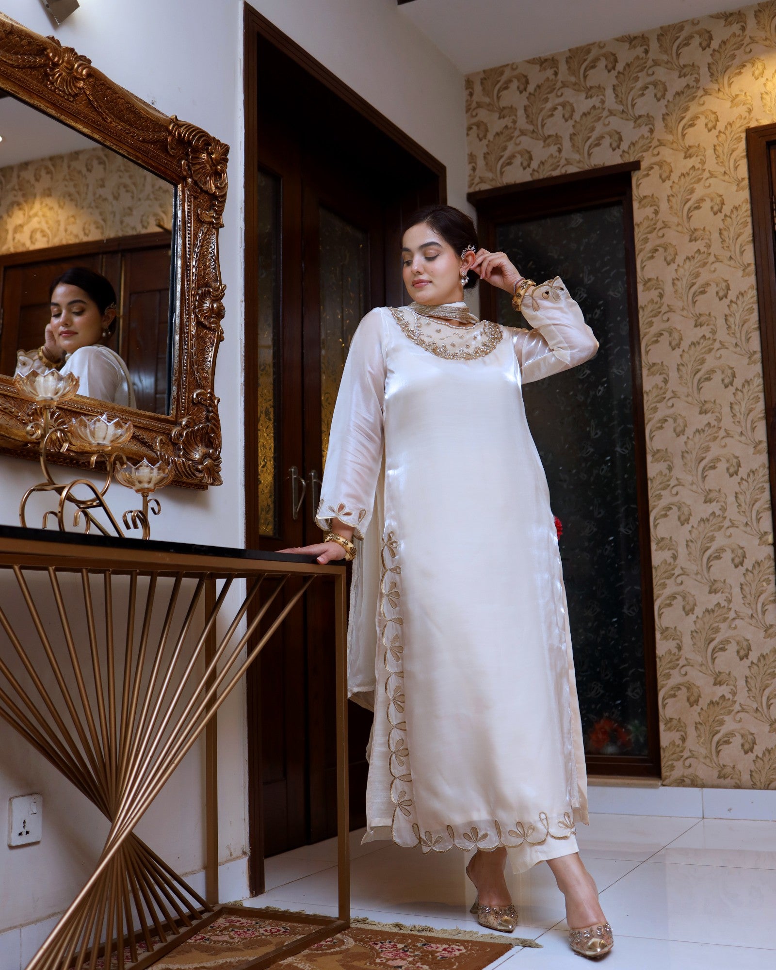 Woman in a white traditional outfit standing in a room with decorative elements.