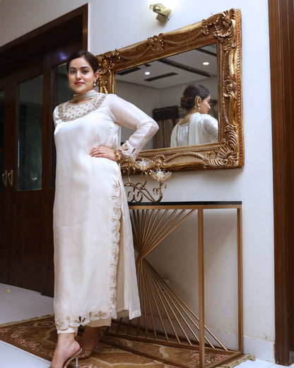 Woman in a white traditional outfit standing in front of a decorative mirror.