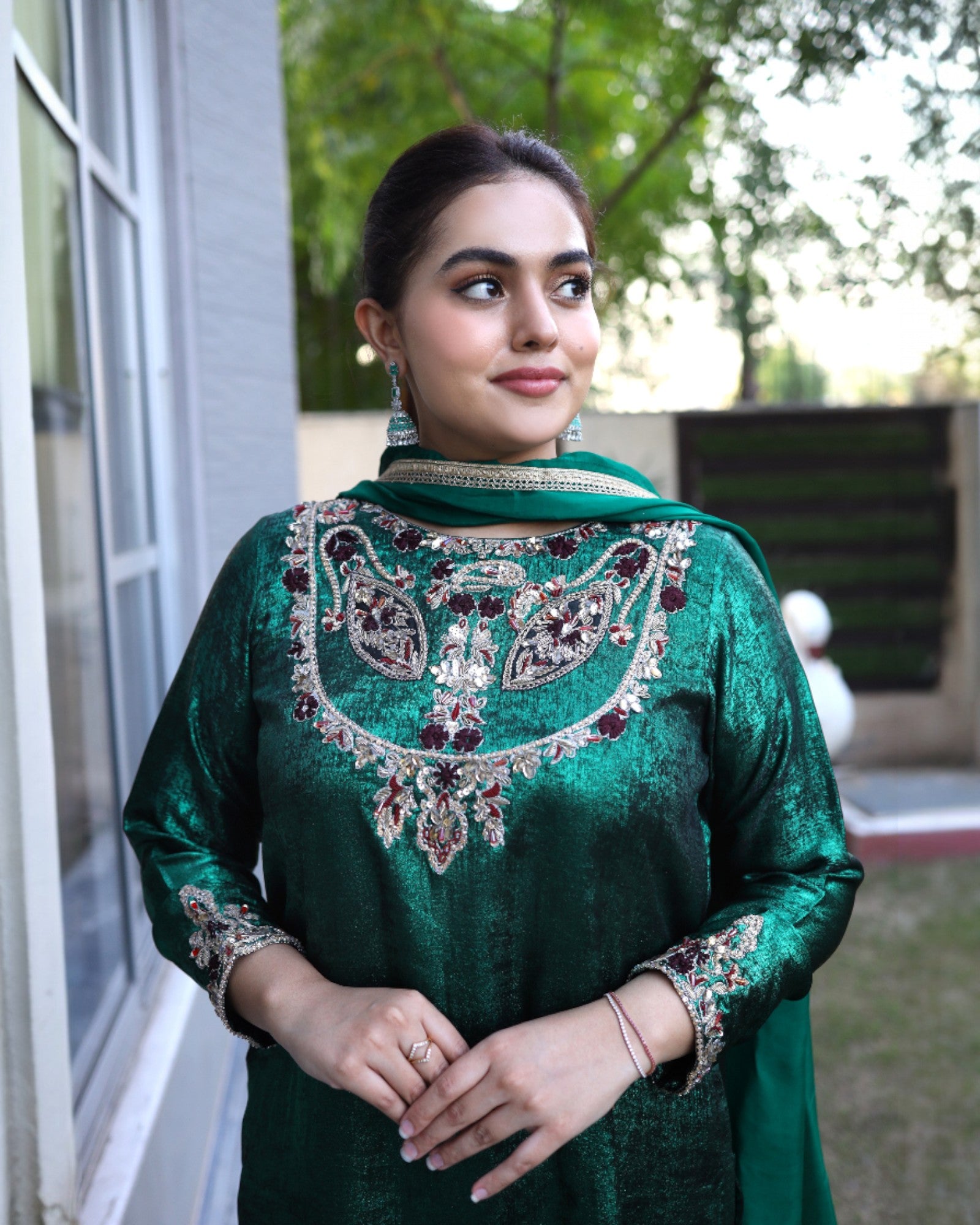 Woman wearing a green traditional outfit with intricate embroidery, standing outdoors.