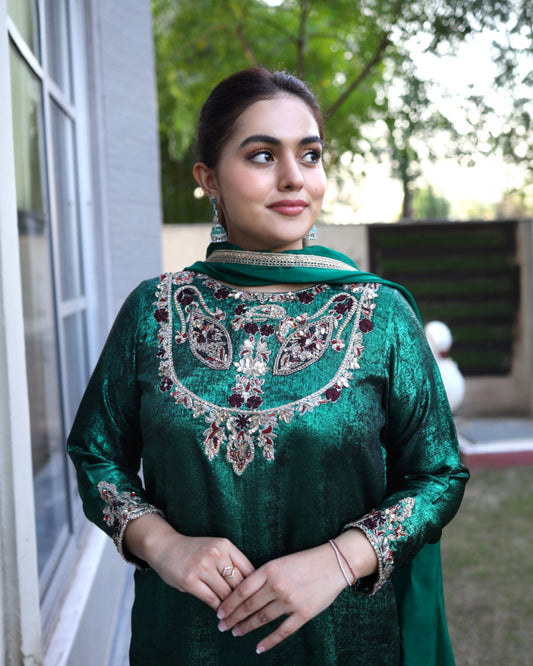 Woman wearing a green traditional outfit with intricate embroidery, standing outdoors.