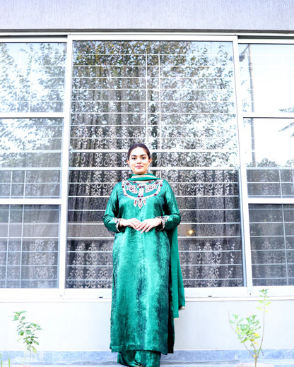 Woman in a green traditional outfit standing in front of a glass window.