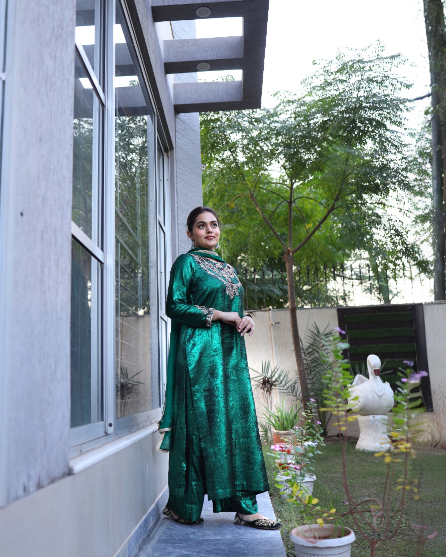 Woman in a green traditional outfit standing in a garden setting.
