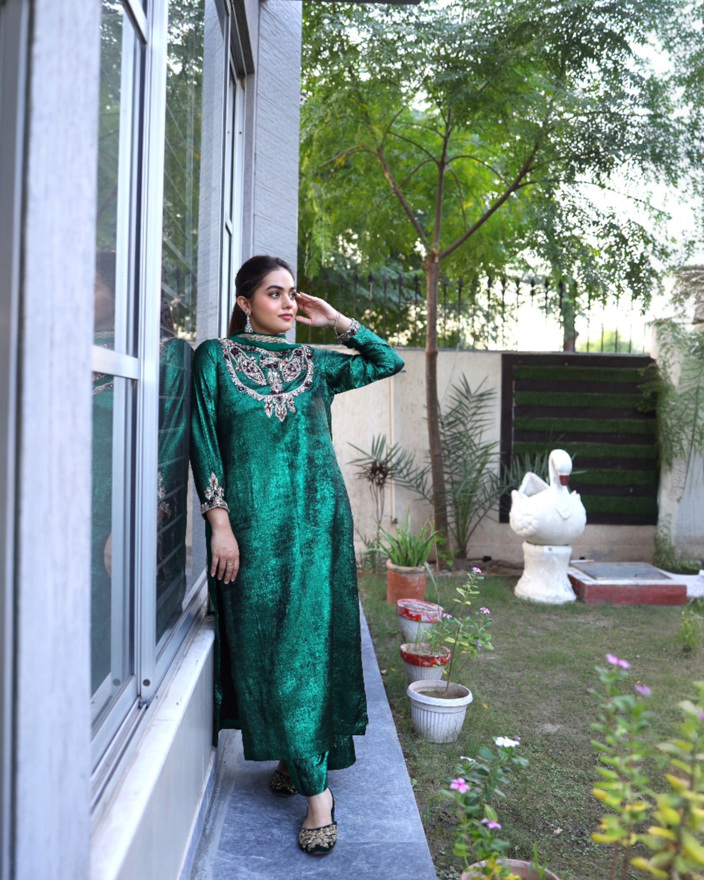 Woman in a green traditional outfit standing on a balcony with a garden view.