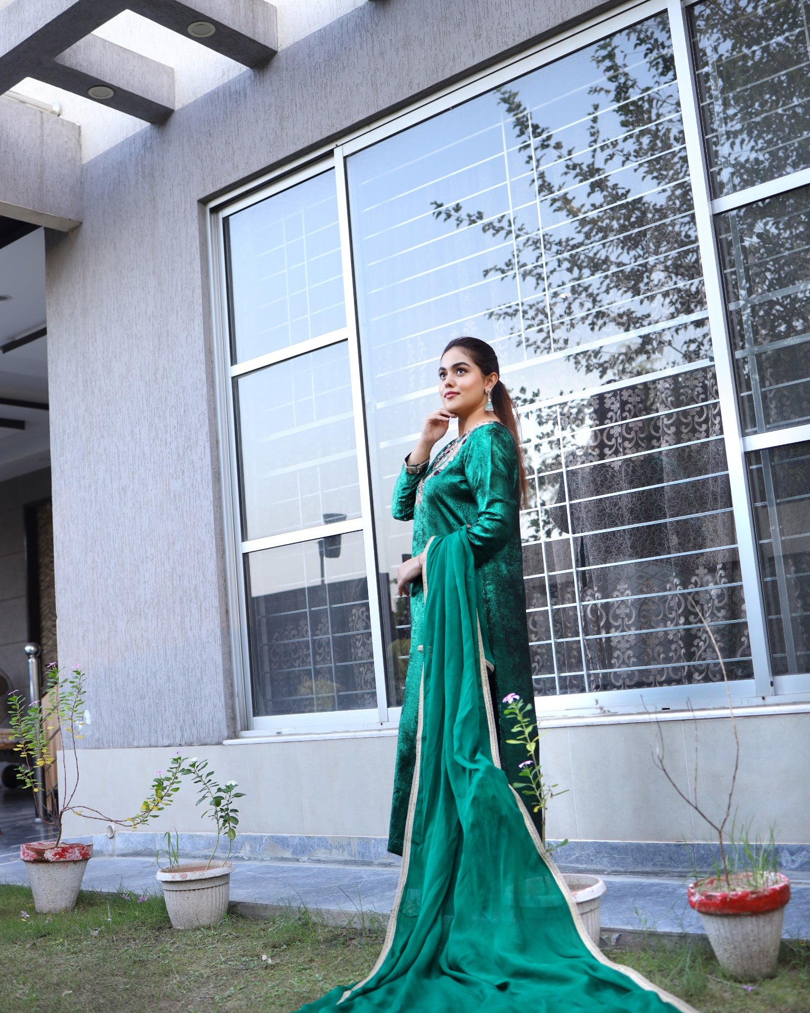 Woman in a green dress standing outside a modern building with large windows.