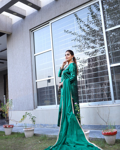 Woman in a green dress standing outside a modern building with large windows.