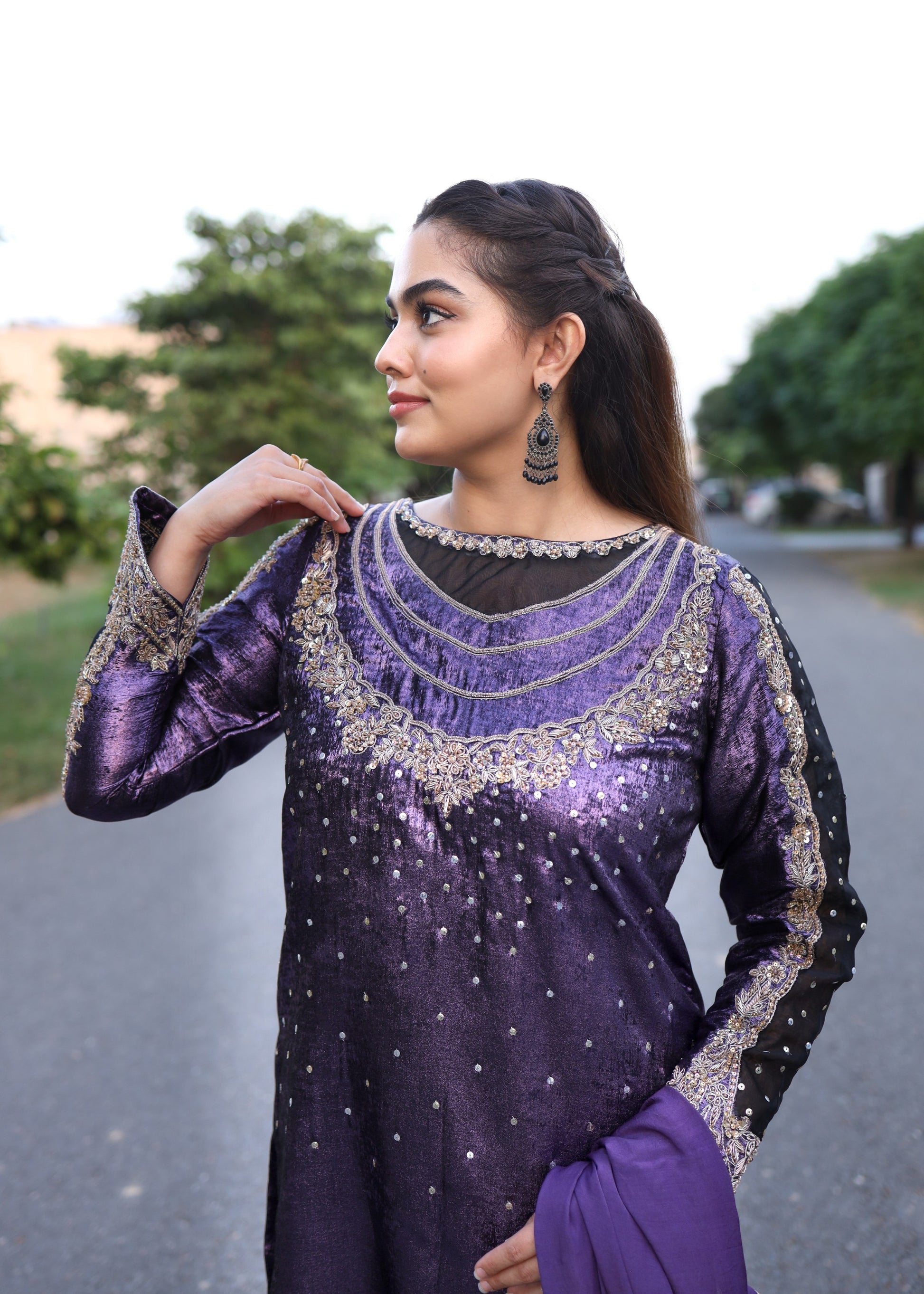 Woman wearing a purple and black traditional outfit with intricate designs outdoors.