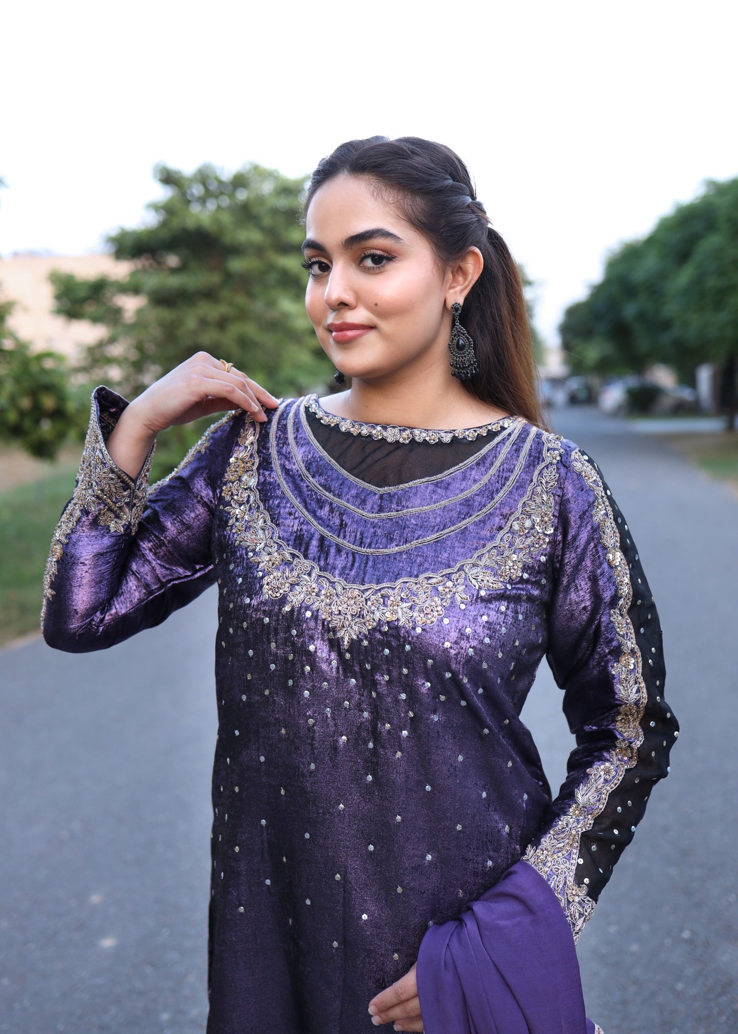 Woman wearing a purple and black embroidered traditional outfit outdoors.