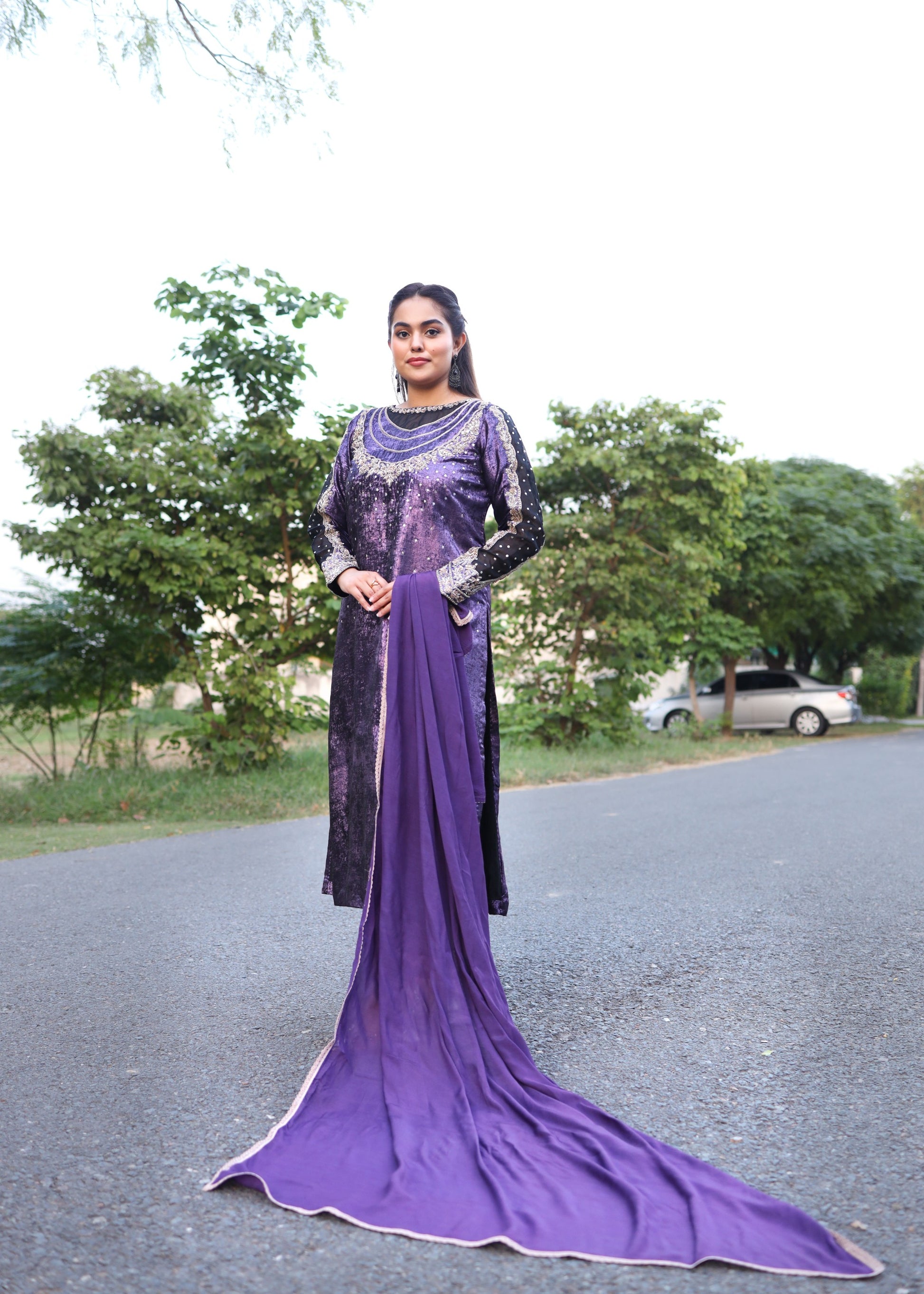 Woman in a long purple dress standing outdoors with trees in the background