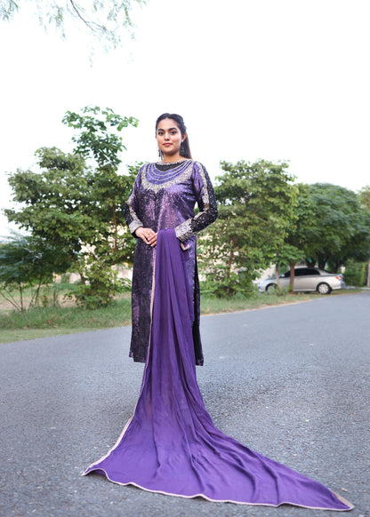 Woman in a long purple dress standing outdoors with trees in the background