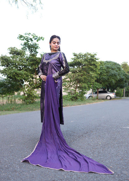 Woman wearing a purple and black traditional outfit standing on a road with trees in the background