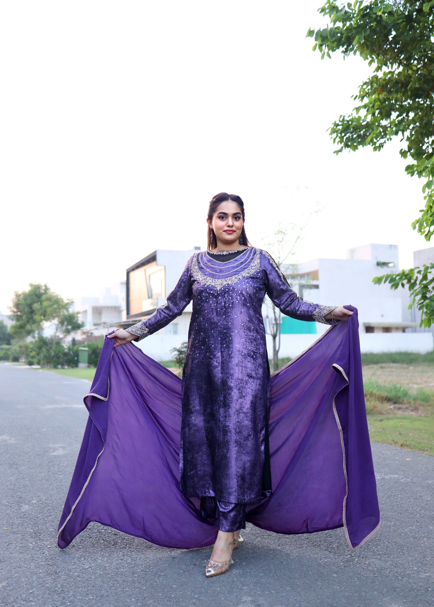 Woman in a purple traditional outfit with a long scarf outdoors.