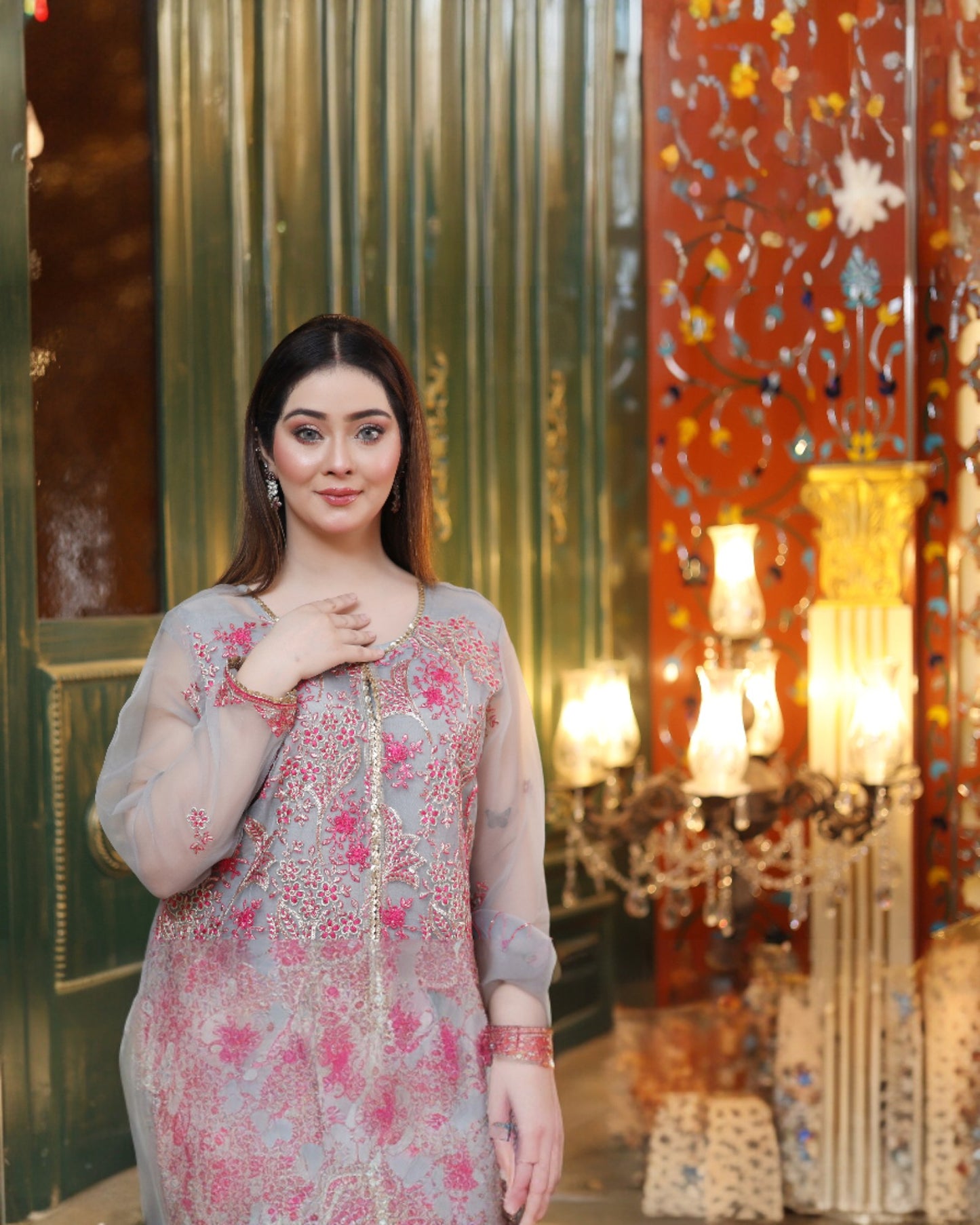 Woman in a floral dress standing in an ornate interior setting with chandeliers.