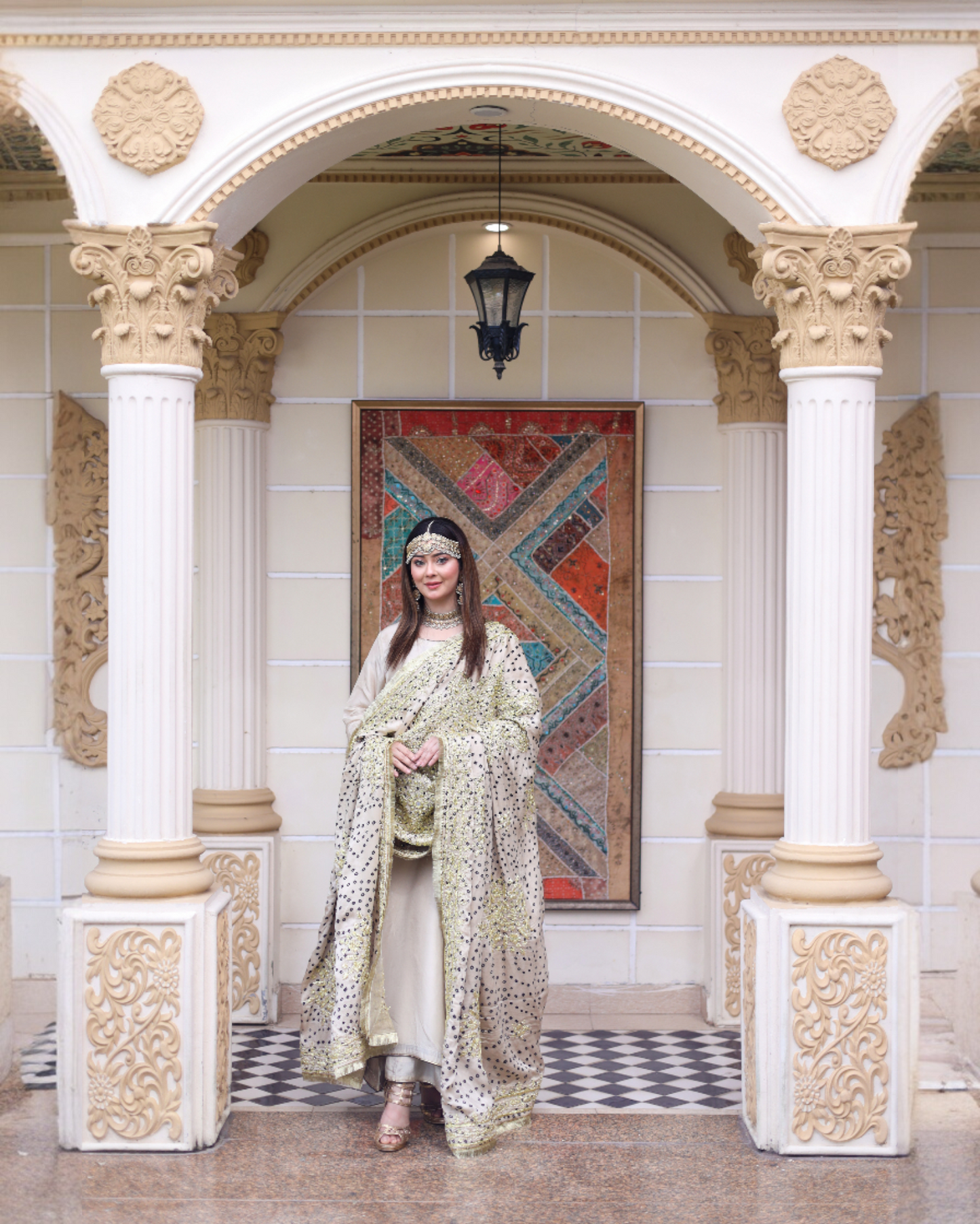 Woman in a floral dress standing in an ornate hall with decorative columns and a colorful tapestry