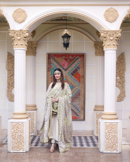 Woman in a floral dress standing in an ornate hall with decorative columns and a colorful tapestry
