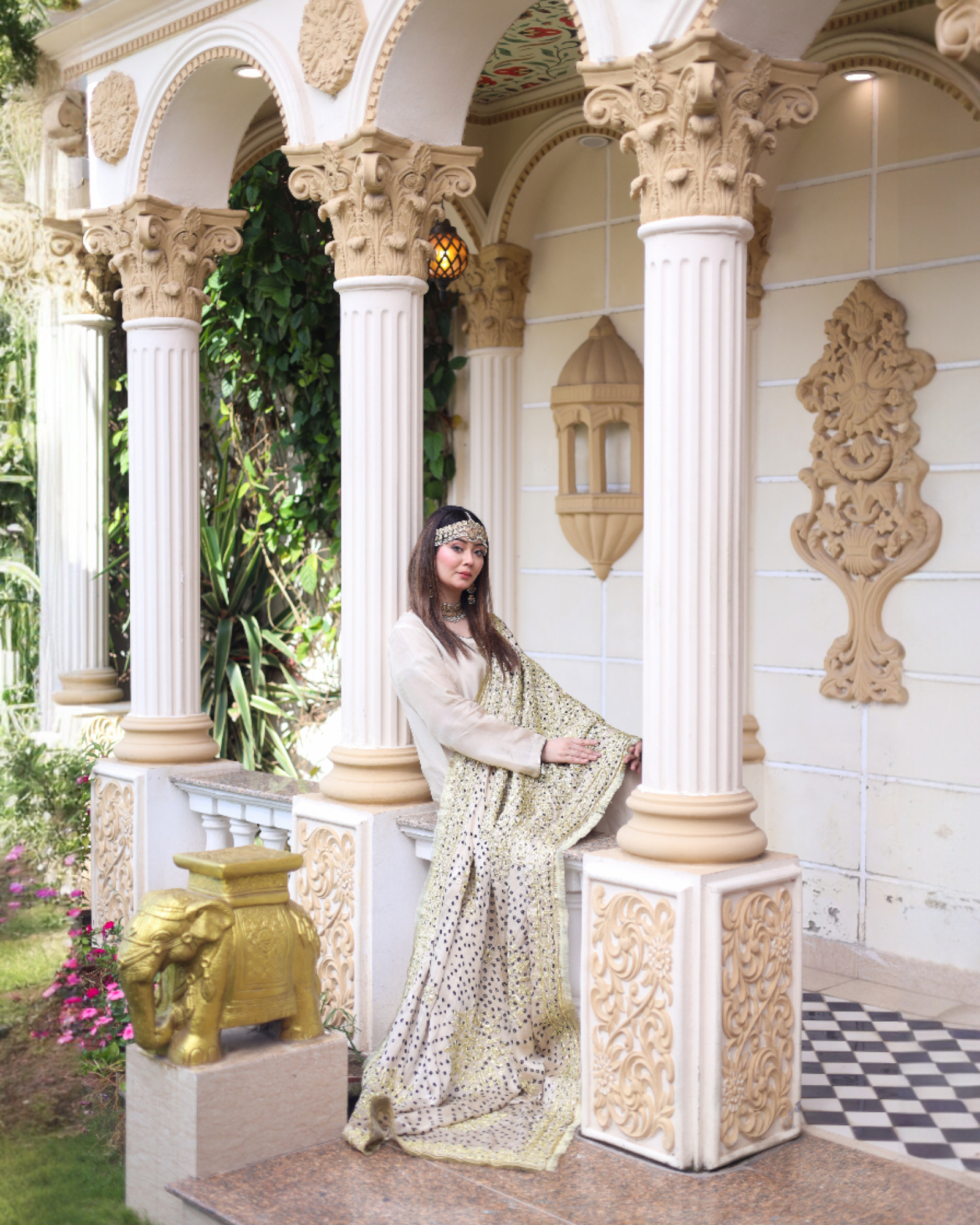Woman in a traditional outfit standing in an ornate architectural setting with columns and decorative elements.