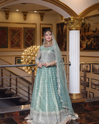 Woman in a traditional green and silver outfit standing in an elegant interior setting.
