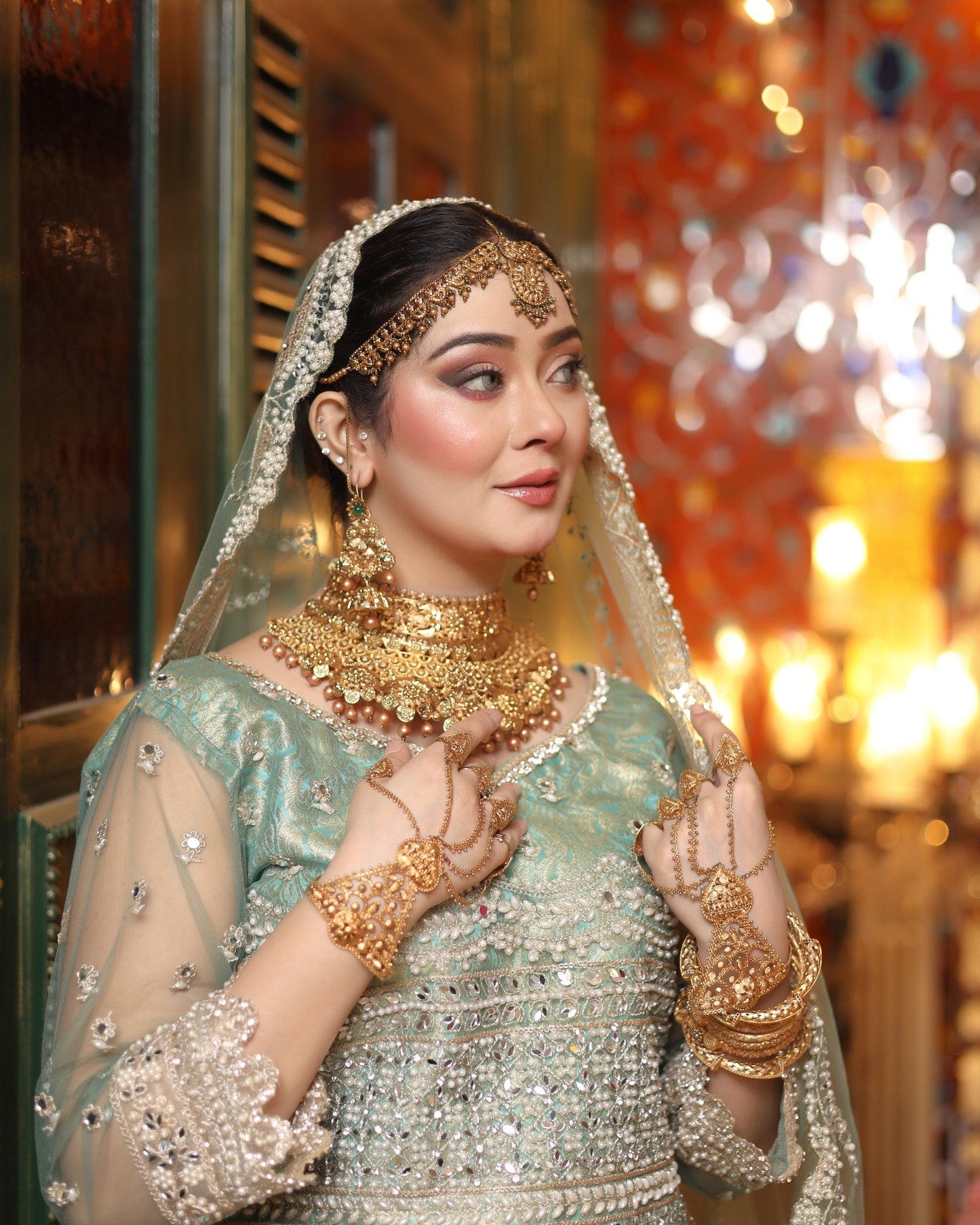 Woman in traditional attire with gold jewelry and a veil in a decorated indoor setting