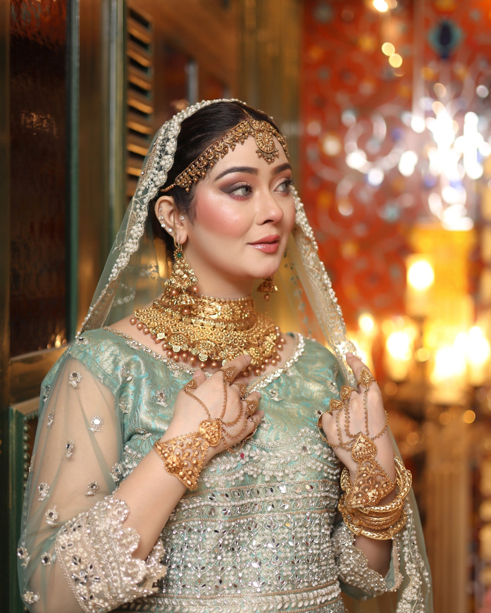 Woman in traditional attire with gold jewelry and a veil in a decorated indoor setting