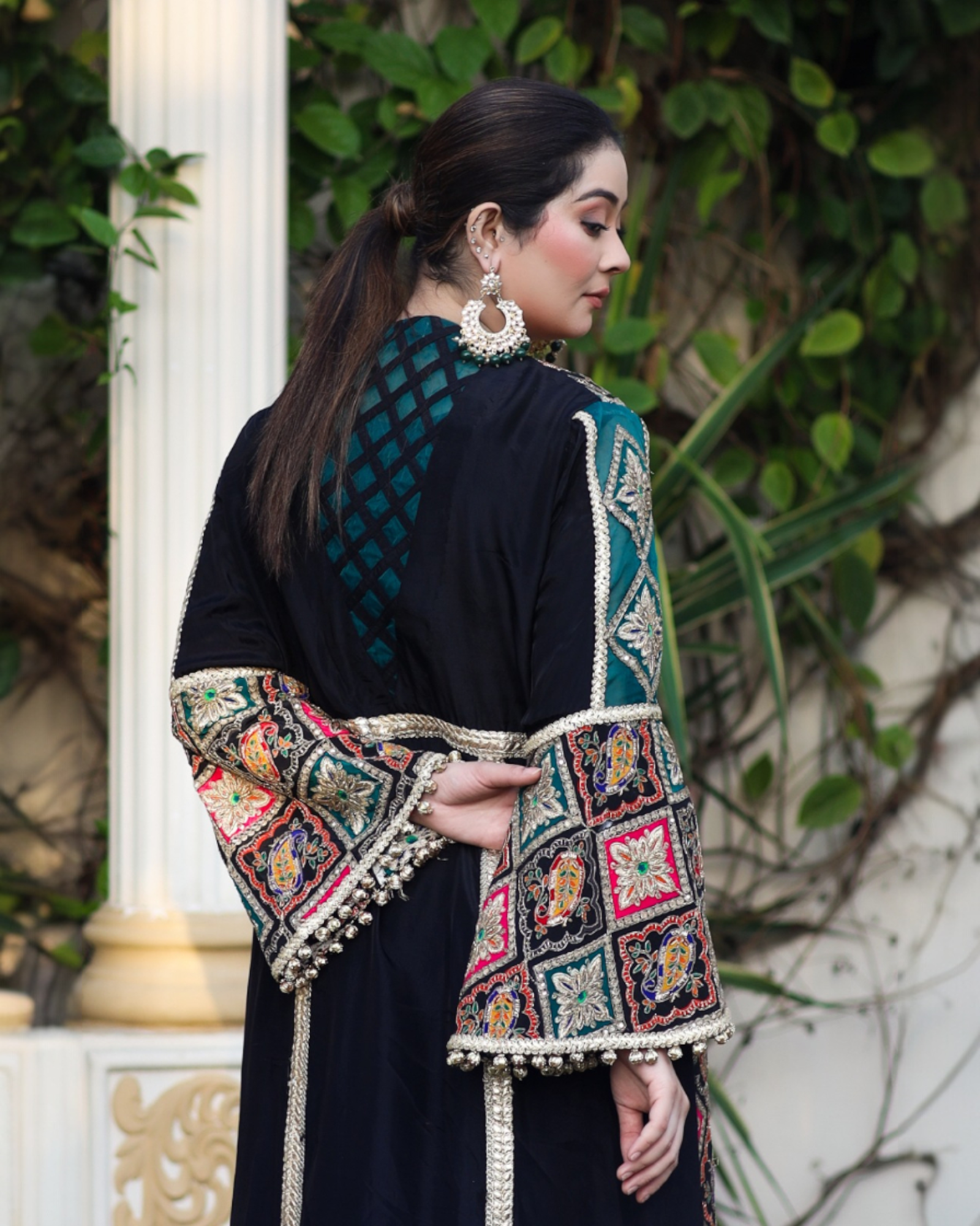 Woman wearing a black outfit with a colorful embroidered shawl outdoors.