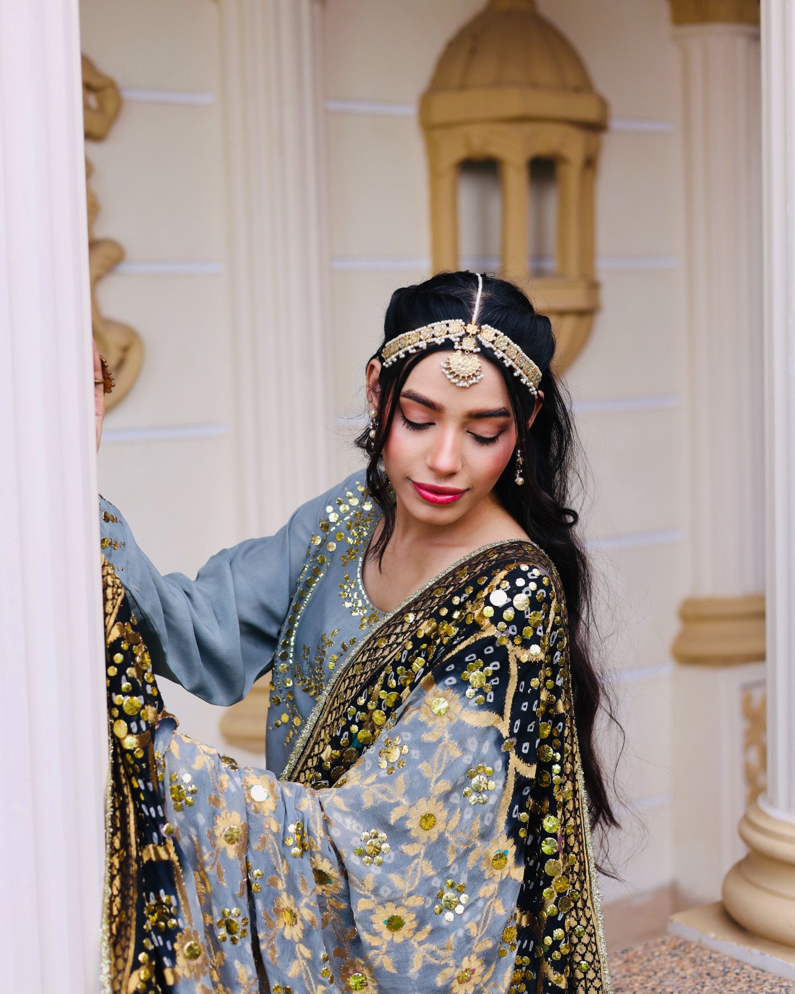 Woman in traditional attire with intricate designs in a decorated interior setting