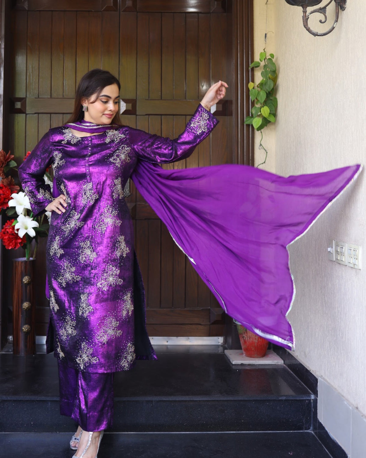 Woman in a purple traditional outfit with a long train, standing indoors.