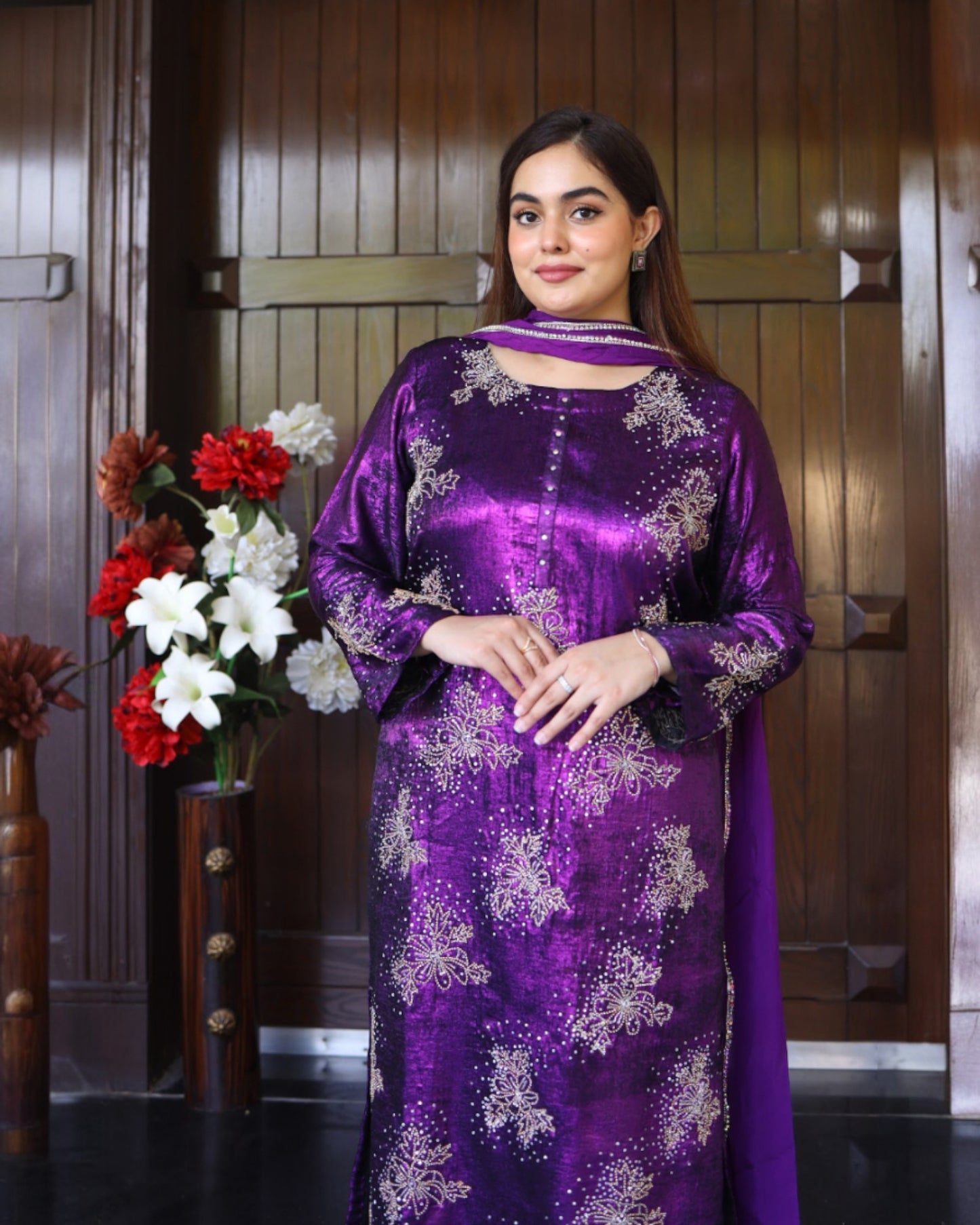 Woman wearing a purple traditional outfit with floral patterns in a room with wooden paneling.