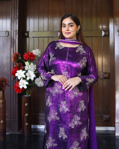 Woman wearing a purple traditional outfit with floral patterns in a room with wooden paneling.