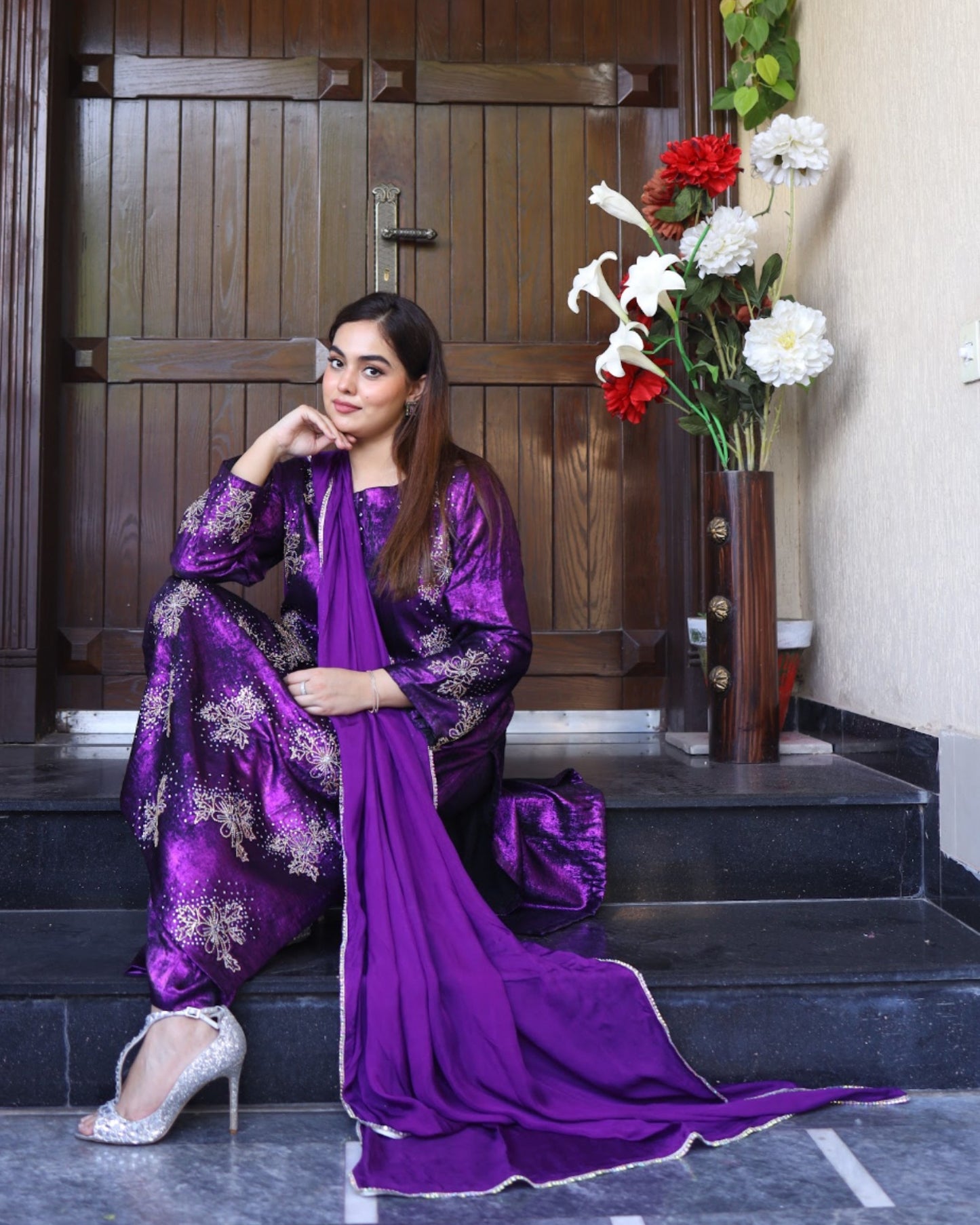 Woman in a purple traditional outfit standing on steps with flowers in the background