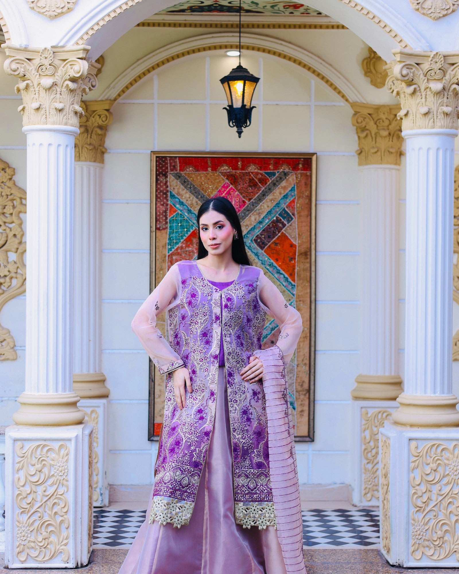 Woman in a purple traditional outfit standing in an ornate interior setting.