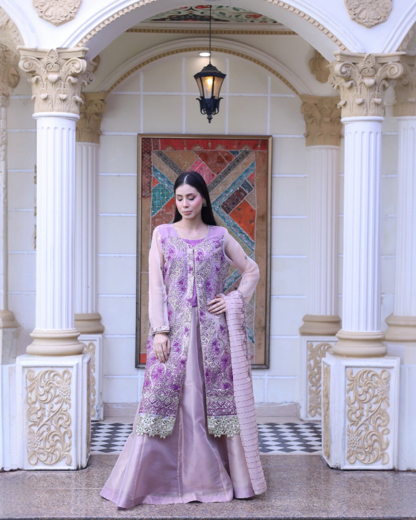 Woman in a pink and purple traditional outfit standing in an ornate hall.