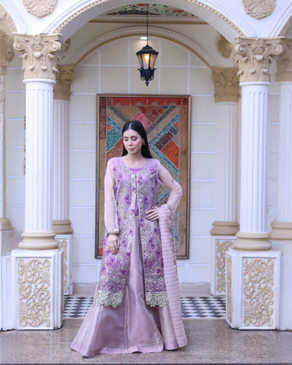 Woman in a pink and purple traditional outfit standing in an ornate hall.