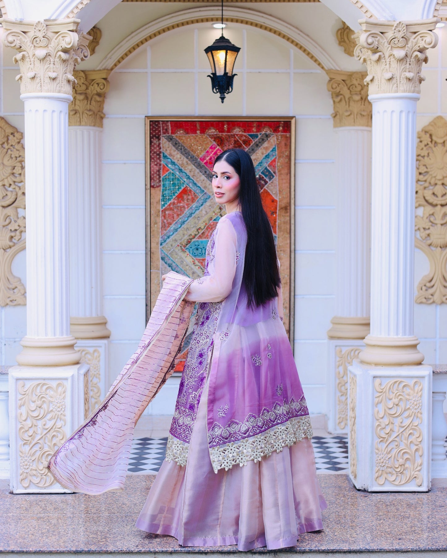 Woman in a purple traditional outfit standing in an ornate architectural setting.
