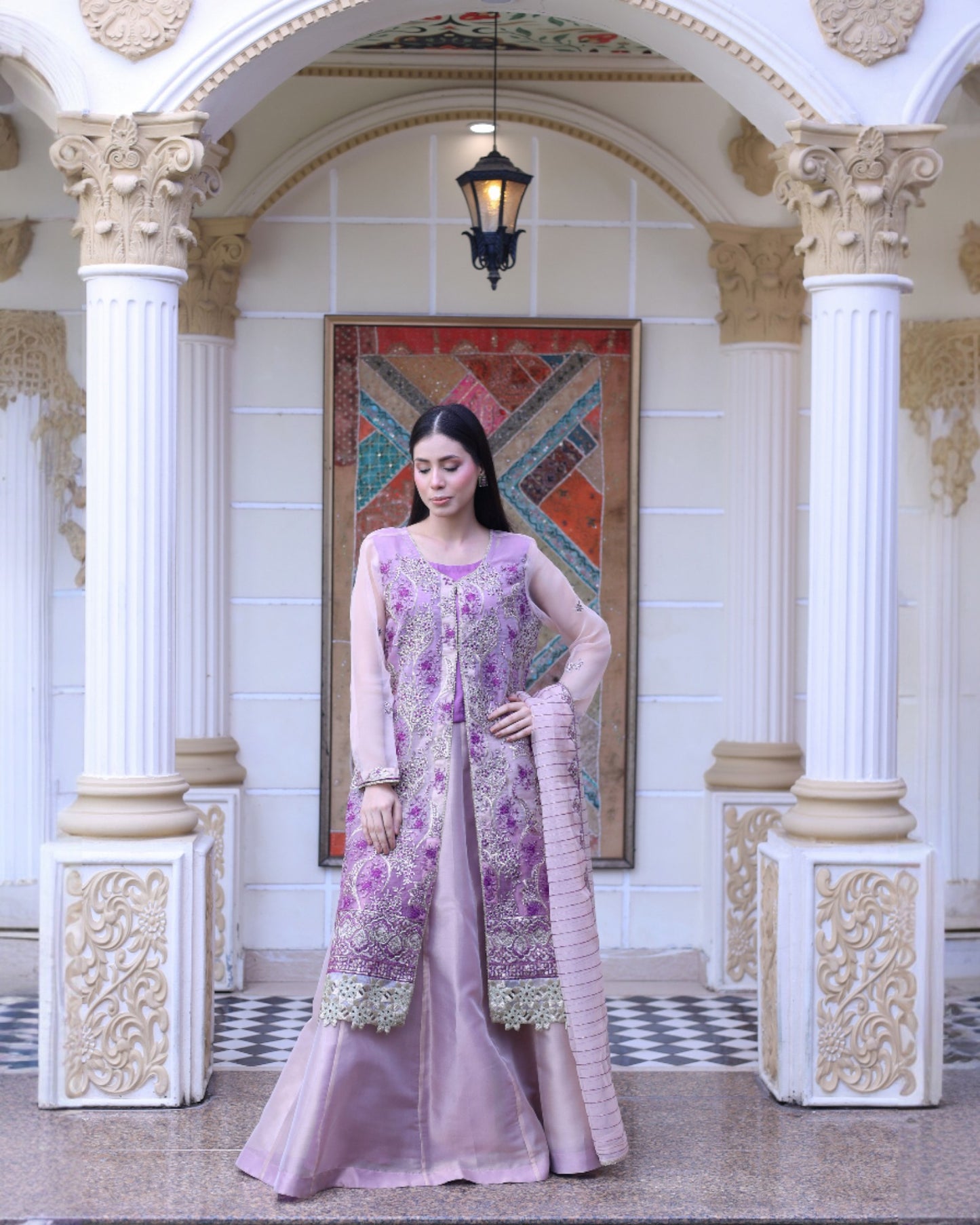 Woman in a pink and purple traditional outfit standing in an ornate hall.