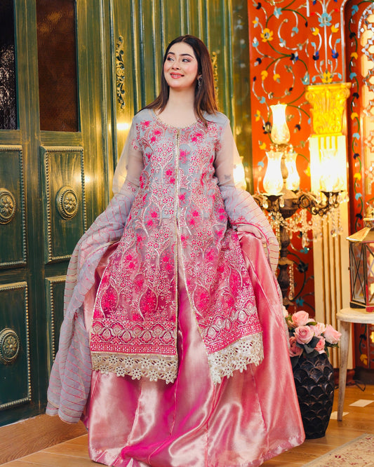 Woman in a pink and white embroidered traditional outfit in a decorated room.