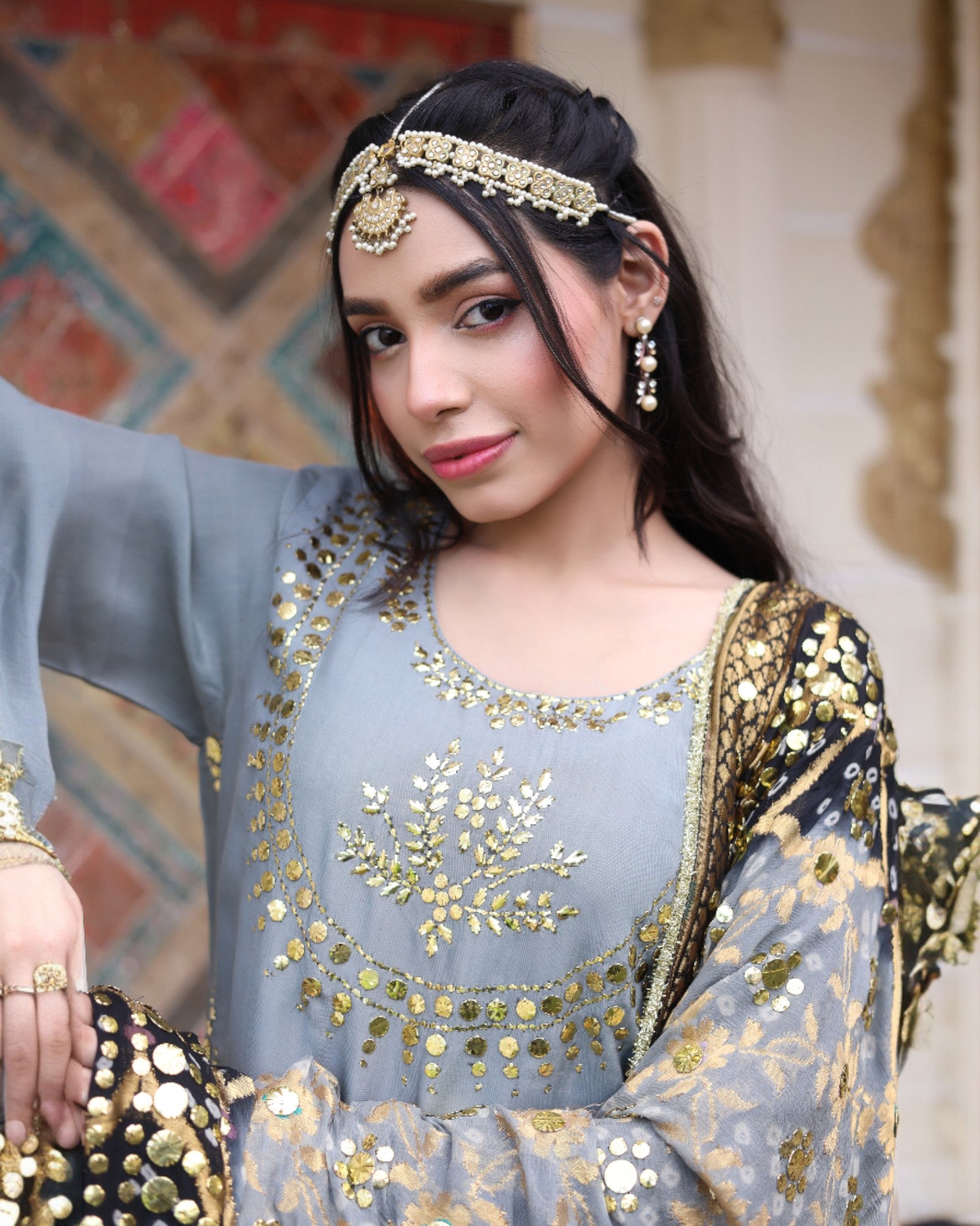 Woman wearing a traditional outfit with gold embroidery and jewelry against a decorative background