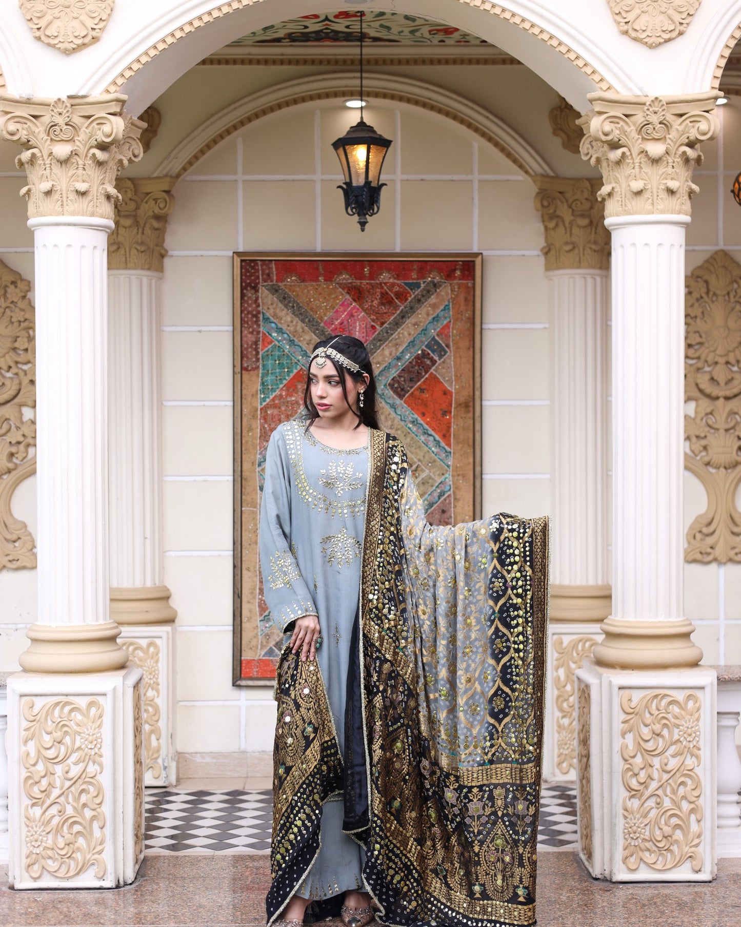 Woman in traditional attire standing in an ornate interior setting with decorative columns and artwork.