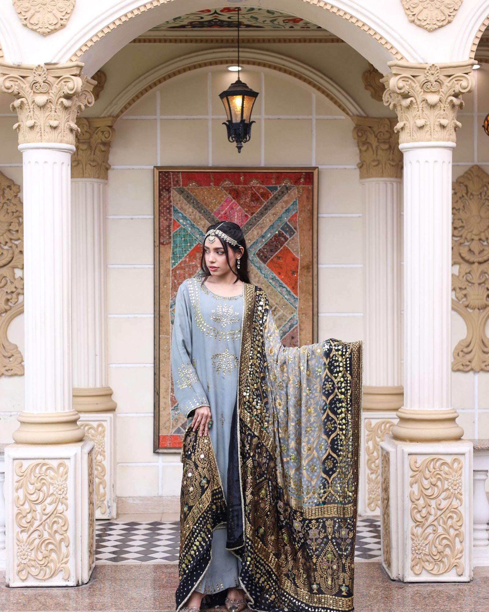 Woman in traditional attire standing in an ornate interior setting with decorative columns and artwork.