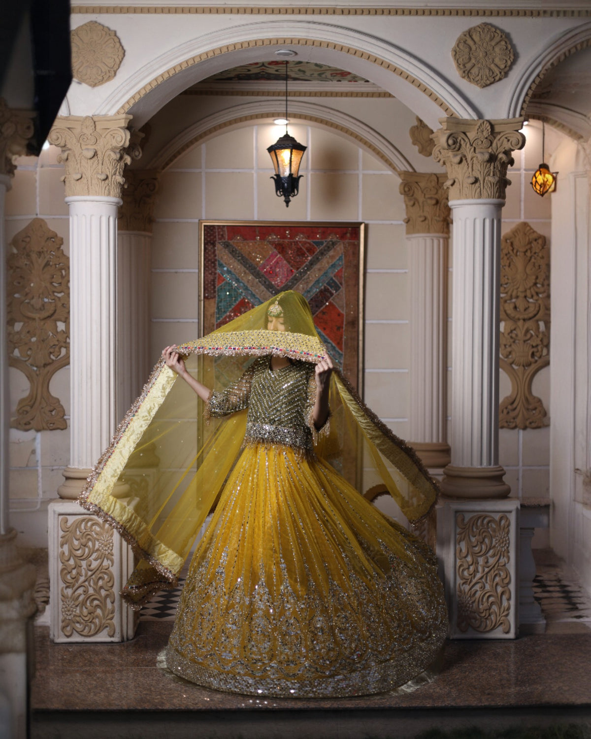 Woman in a yellow and silver traditional outfit standing in an ornate room.